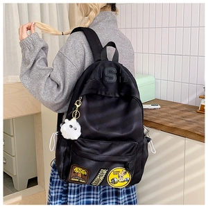 Detail of black canvas backpack showing USH embossed logo and cartoon badges with fur ball