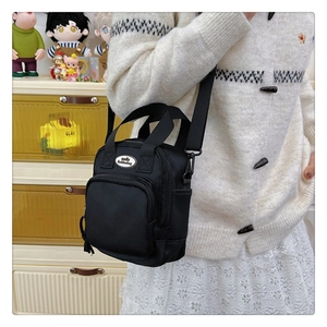 Detail of black mini crossbody bag with silver smile fashionbag emblem and adjustable strap