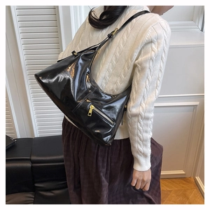 Detail der glänzenden schwarzen Knödeltasche mit Goldreißverschluss auf weißem Pullover