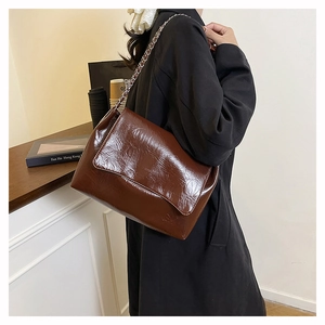 Sac à bandoulière en cuir ciré marron avec chaîne argentée porté par un mannequin en scène
