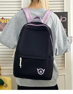 Detail of black backpack with purple straps and M logo patch shown in a lifestyle setting