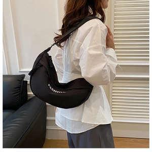 Detail of a black crescent crossbody bag with white FASHION lettering on a model