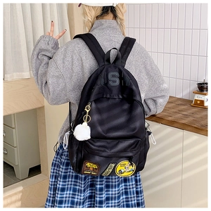Detail of black nylon backpack with decorative embroidery patches and white fuzzy pompom charm