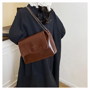 Détail du sac à bandoulière en cuir brillant marron foncé avec chaîne porté par un modèle