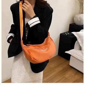 On-body shot of a bright orange crescent crossbody bag with white FASHION lettering