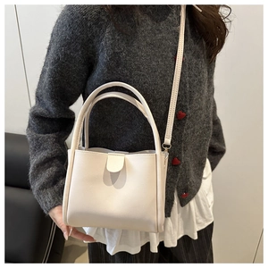 Detailed view of a white minimalist bucket bag featuring heart clasp and round handles