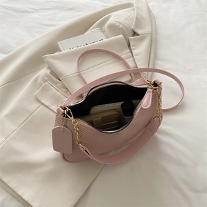 Pink woven underarm bag with gold chain and strap on a beige blazer background