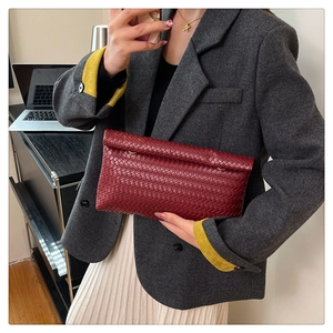 Détail de la texture tressée bordeaux d'un sac à bandoulière rectangulaire avec anneaux