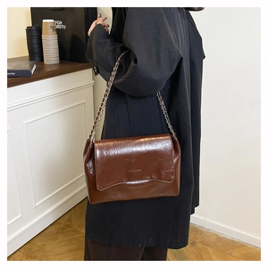 Détail d'un sac bandoulière chaîne marron foncé à texture froissée porté par un mannequin
