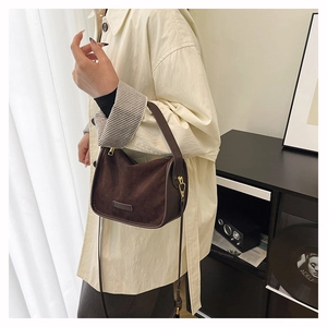 Detail of dark brown suede Boston bag with gold hardware worn with a beige trench coat