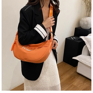 Model wearing a bright orange crescent crossbody bag with white FASHION lettering