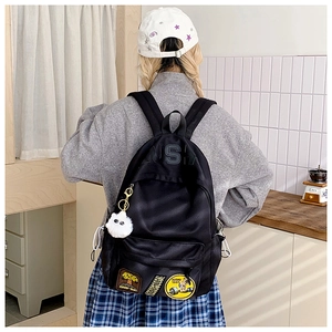 Detail view of black nylon backpack with vintage patches and a fluffy white pompom charm