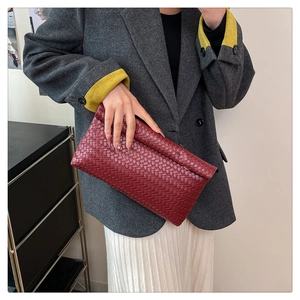 Gros plan d'une pochette enveloppe en cuir tressé bordeaux portée avec un costume