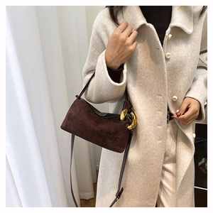 Détail du sac en daim marron chocolat avec boucle noeud dorée sur un manteau beige