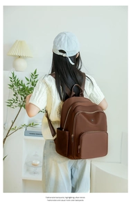 Brown multi-pocket nylon backpack shown on model in a cozy indoor lifestyle setting