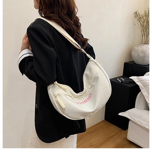 Detail view of a white half-moon canvas bag featuring pink lettering and woven zipper pull