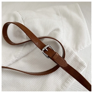 Detail shot of a sleek brown leather belt with a silver buckle on a textured background