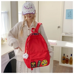 Detail of red canvas backpack with KUSHU 1981 patches and cute plush ball pendant
