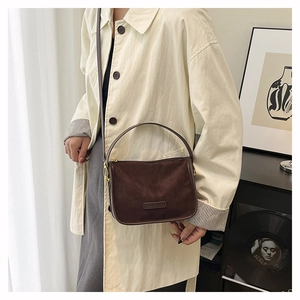 Close-up of a dark brown suede crossbody bag with rounded handles and a matte texture