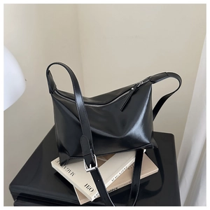 Detail of black glossy leather tote bag with silver buckle and adjustable shoulder strap