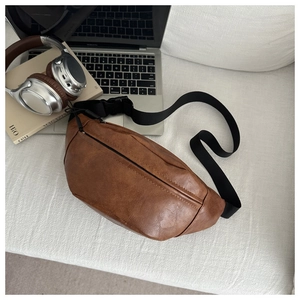 Top view of brown PU leather crescent sling bag on a white sofa with lifestyle props