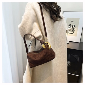 Détail d'un sac en daim marron avec boucle dorée porté sur un long manteau beige