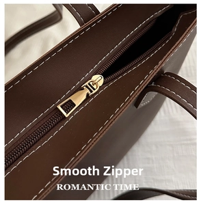 Detail of dark brown leather tote bag with smooth gold zipper and white topstitching