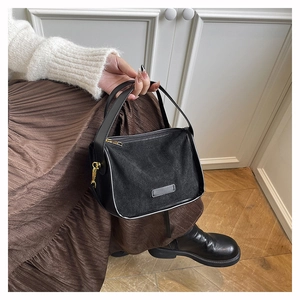 Detail of a minimalist black tote bag with gold hardware held by a model in brown dress