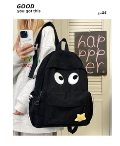Detail of black corduroy backpack featuring large eye embroidery and yellow star charm