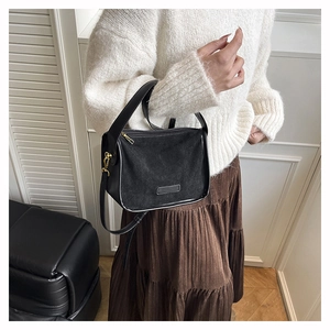 Detail of black faux suede shoulder bag featuring gold hardware and adjustable strap