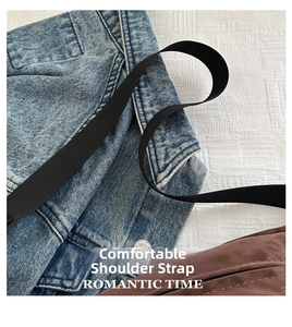Detail of a wide black nylon shoulder strap attached to a blue denim bag with metal buttons