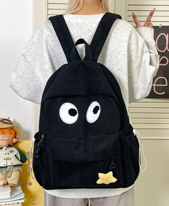 Close-up of black corduroy backpack featuring big eye patches and yellow star charm