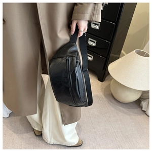 Detail of black pebbled leather sling bag with adjustable strap worn with casual coat