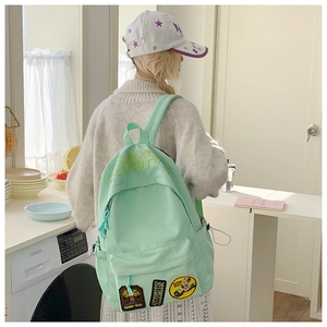 Mint green canvas backpack with creative embroidery patches worn in a home kitchen setting