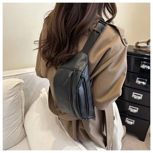 Detail of minimalist black leather chest bag with adjustable strap worn by model