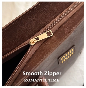 Detail view of smooth metal zipper and textured litchi leather on brown tote bag