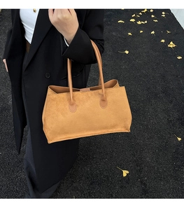 Detail view of large camel suede tote bag on autumn ground with yellow leaves