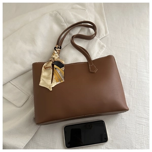 Brown leather tote bag showing size scale next to a smartphone and floral silk scarf charm