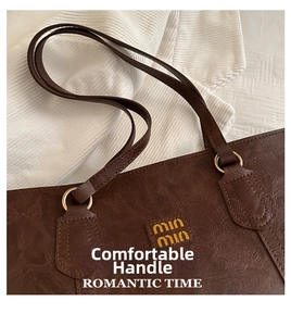 Detail of a brown leather tote bag showing slim straps and gold metal ring hardware