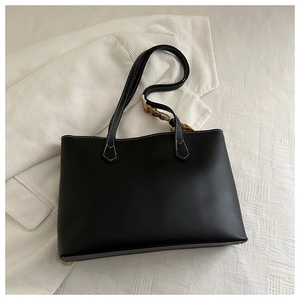 Detail of black tote bag with white contrast stitching and a patterned silk scarf handle
