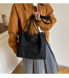 Detail of black suede tote bag featuring distinctive woven leather handles and gold logo