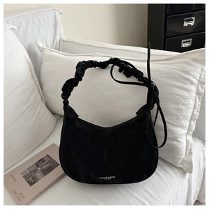 Detail view of black hobo bag with cloud pleat handle and fashion logo on white sofa