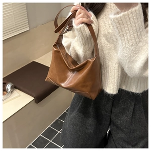 Brown leather dumpling bag with soft drape and adjustable strap shown in a lifestyle setting