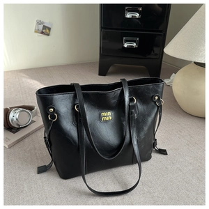 Detail of glossy black leather tote bag with gold brand emblem and side drawstring charms