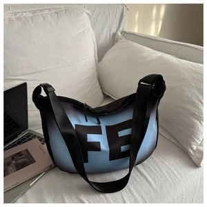 Détail du sac bandoulière dégradé bleu-noir avec imprimé lettre FE sur un canapé blanc