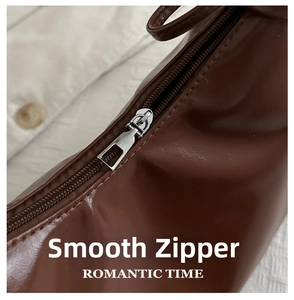 Close-up of smooth silver metal zipper on a textured dark brown oily leather handbag