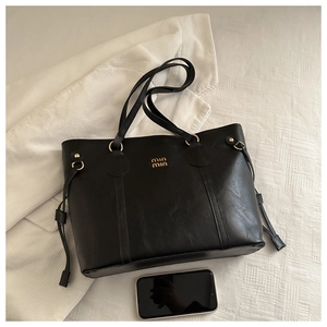 Detail view of large black tote bag with gold logo, side drawstring and mobile phone for scale