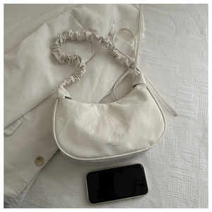Detail of white marble-patterned hobo bag with pleated shoulder strap on fabric background