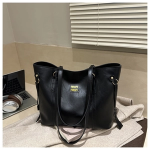 Detail of black tote bag featuring pebbled faux leather and golden logo on surface