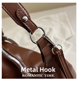 Detail of silver metal hook and strap stitching on a brown leather dumpling bag